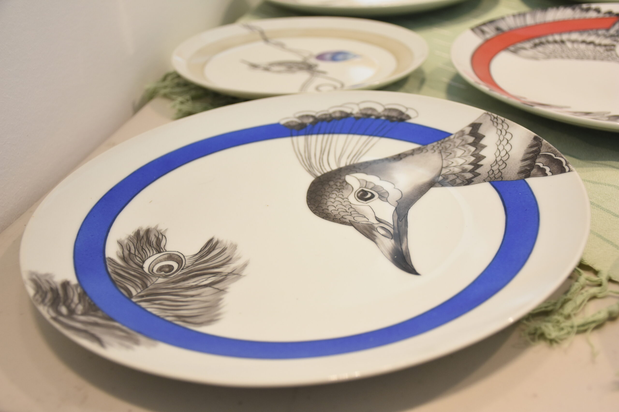 Une assiette en porcelaine peinte. Le dessin représenté est un paon en noir et blanc avec un liseré bleu sur le bord de l'assiette