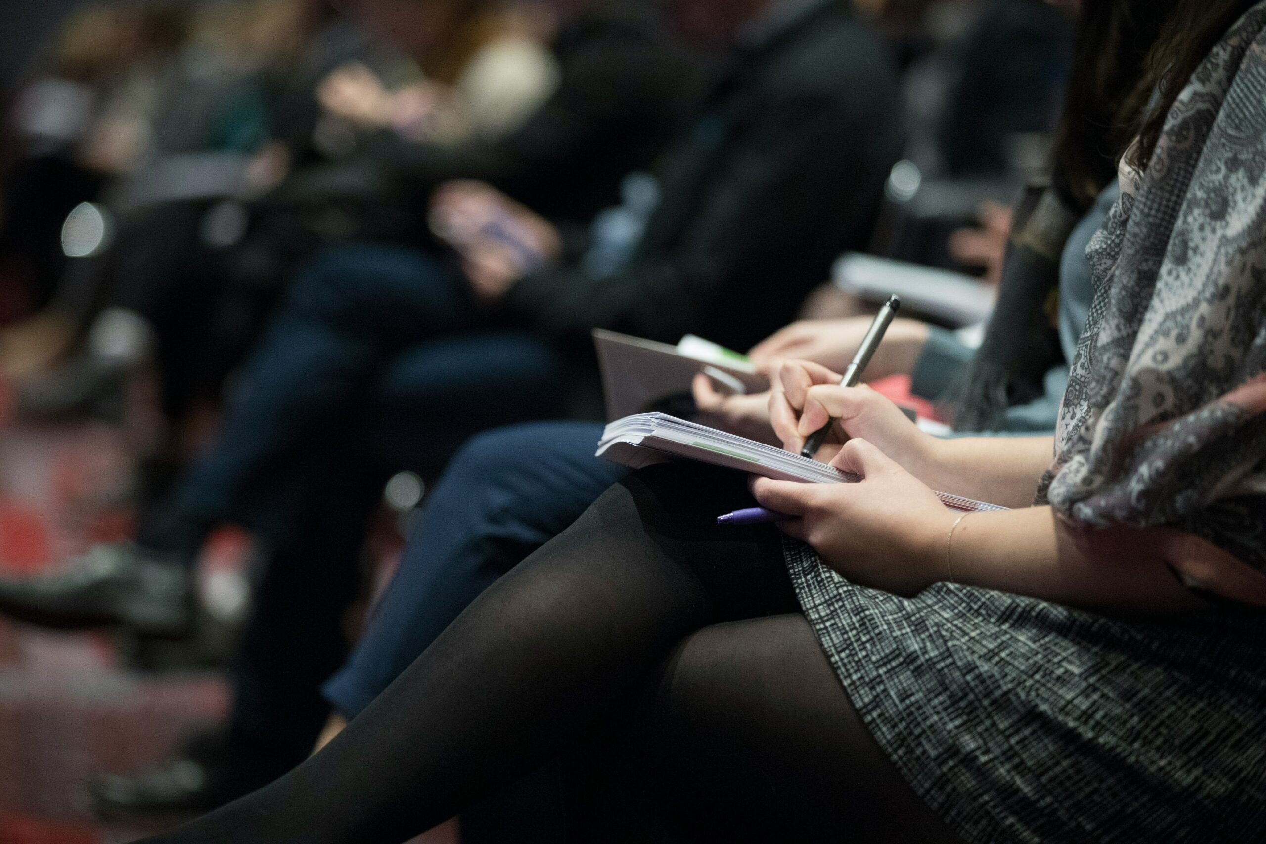 Une femme assise à une conférence entrain de prendre des notes dans son carnet