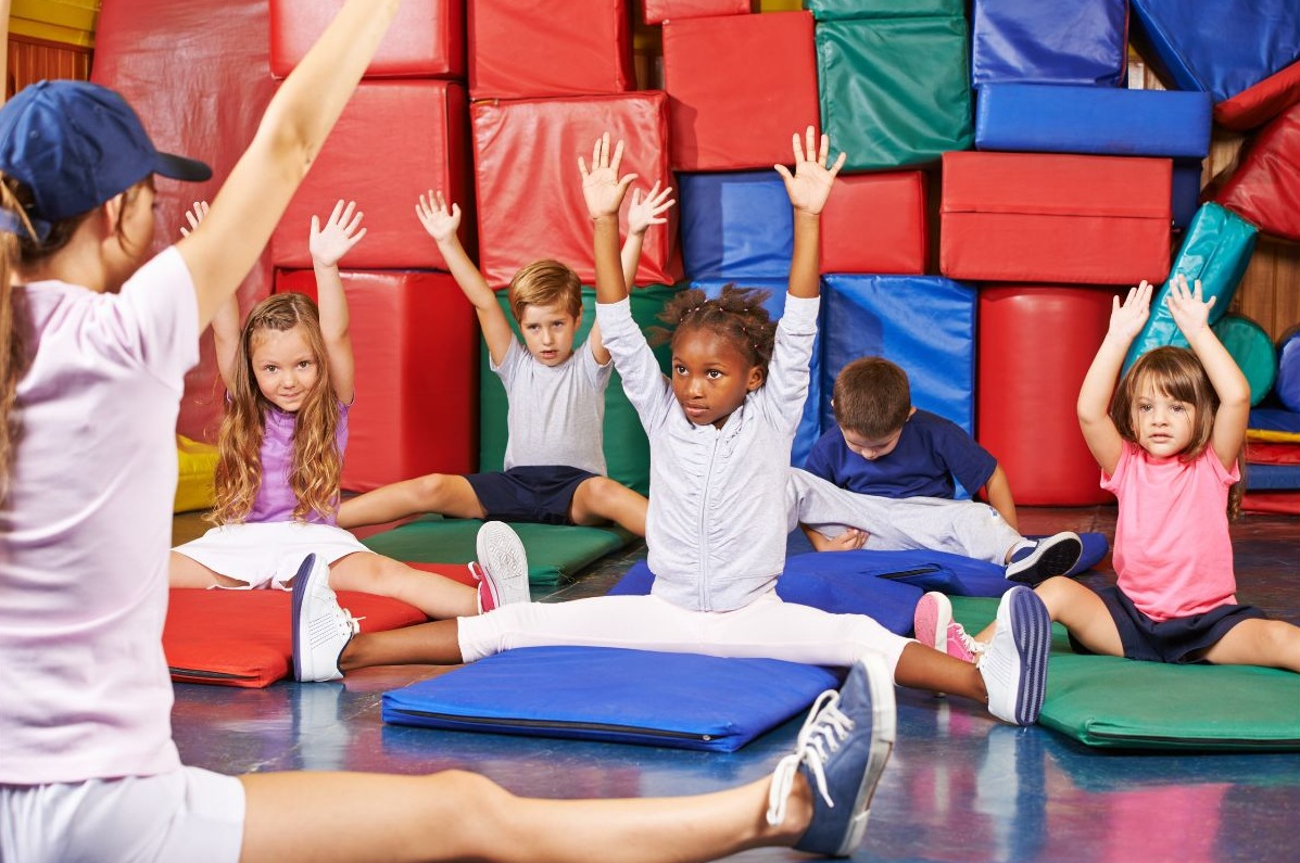 Des enfants assis et les mains en l'air entrain de faire de la gym sportive